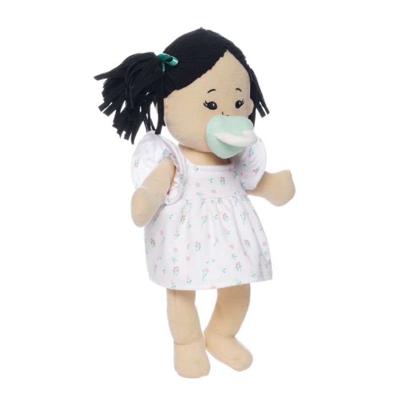 Soft doll with black hair and light beige skin wearing a dress with a light green magnetic pacifier on the doll's face while standing.