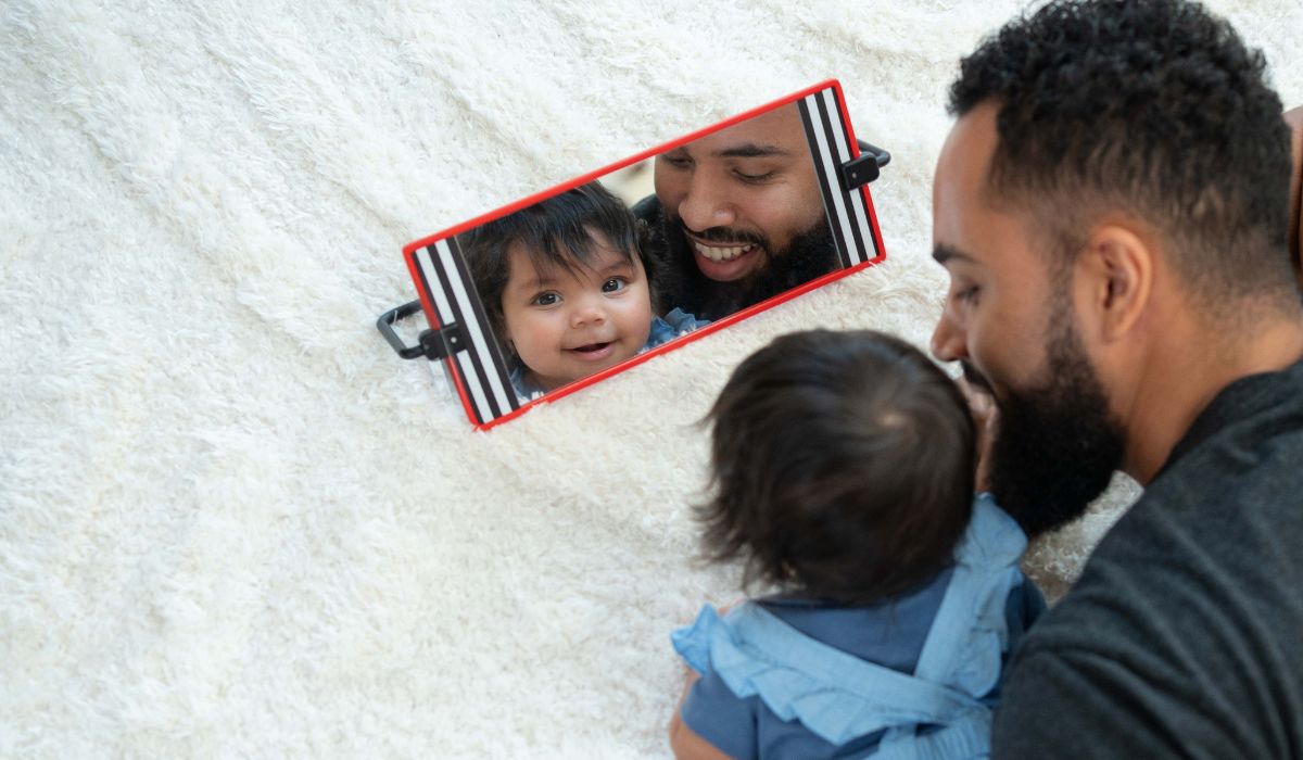 Baby and father bonding during tummy time while looking into a high-contrast sensory mirror toy.