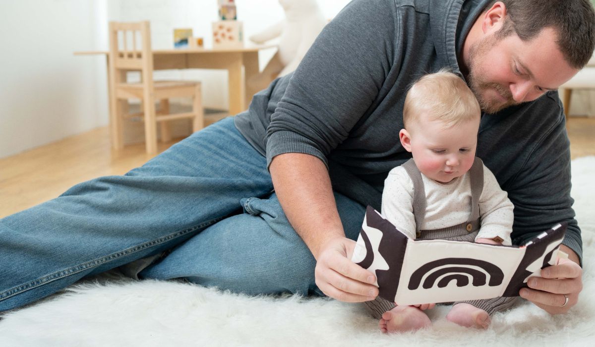 Father and baby reading a soft high-contrast cloth book together during floor time in a cozy playroom.