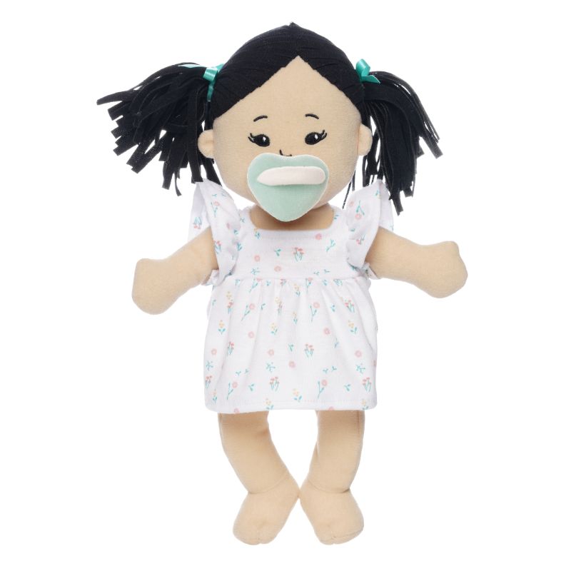 Soft doll with black hair and light beige skin wearing a dress with a light green magnetic pacifier on the doll's face while standing.