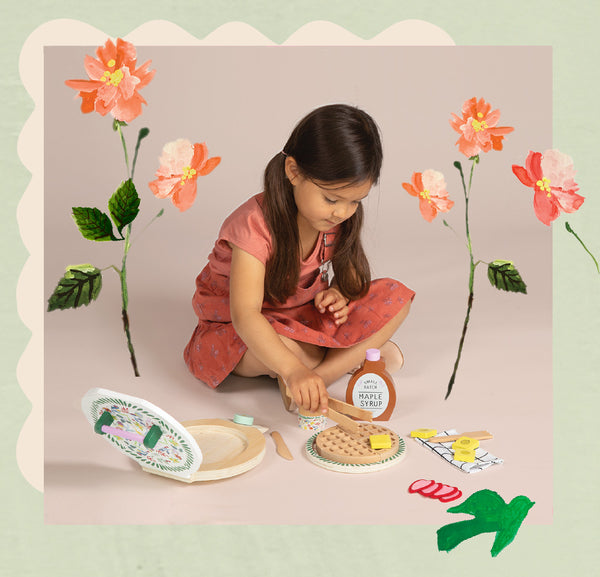 Little girl sitting on ground, playing with waffle and butter toys