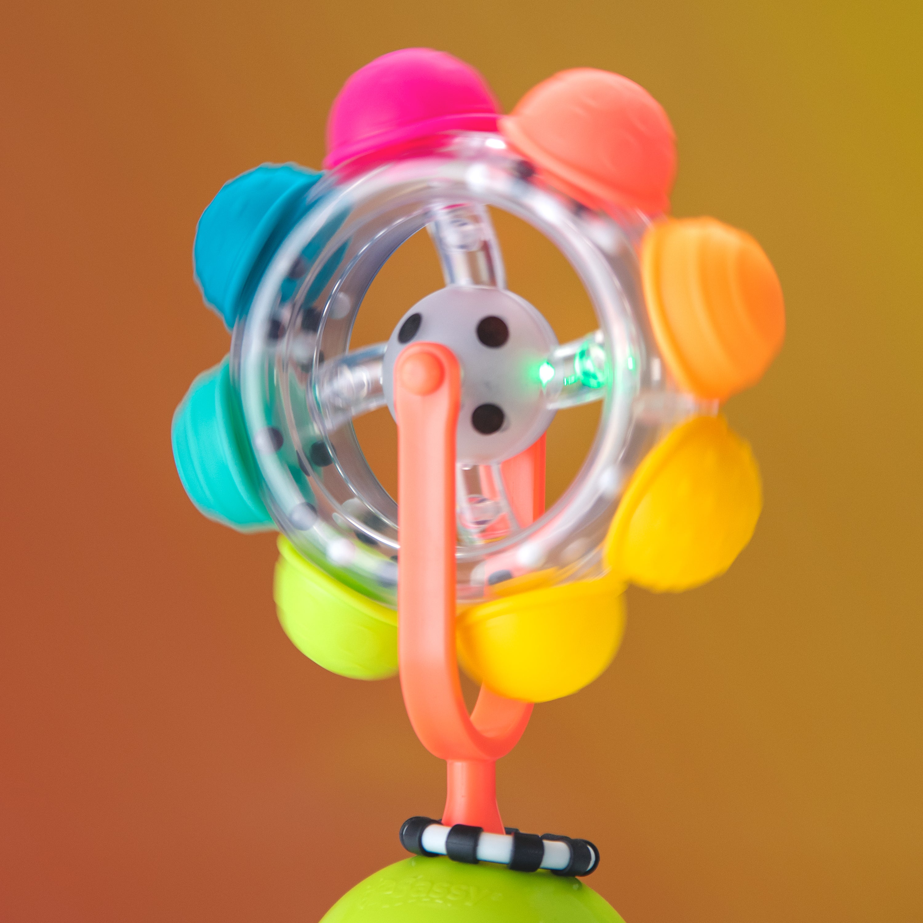 light up rainbow reel toy, lighting up green, on an orange background.