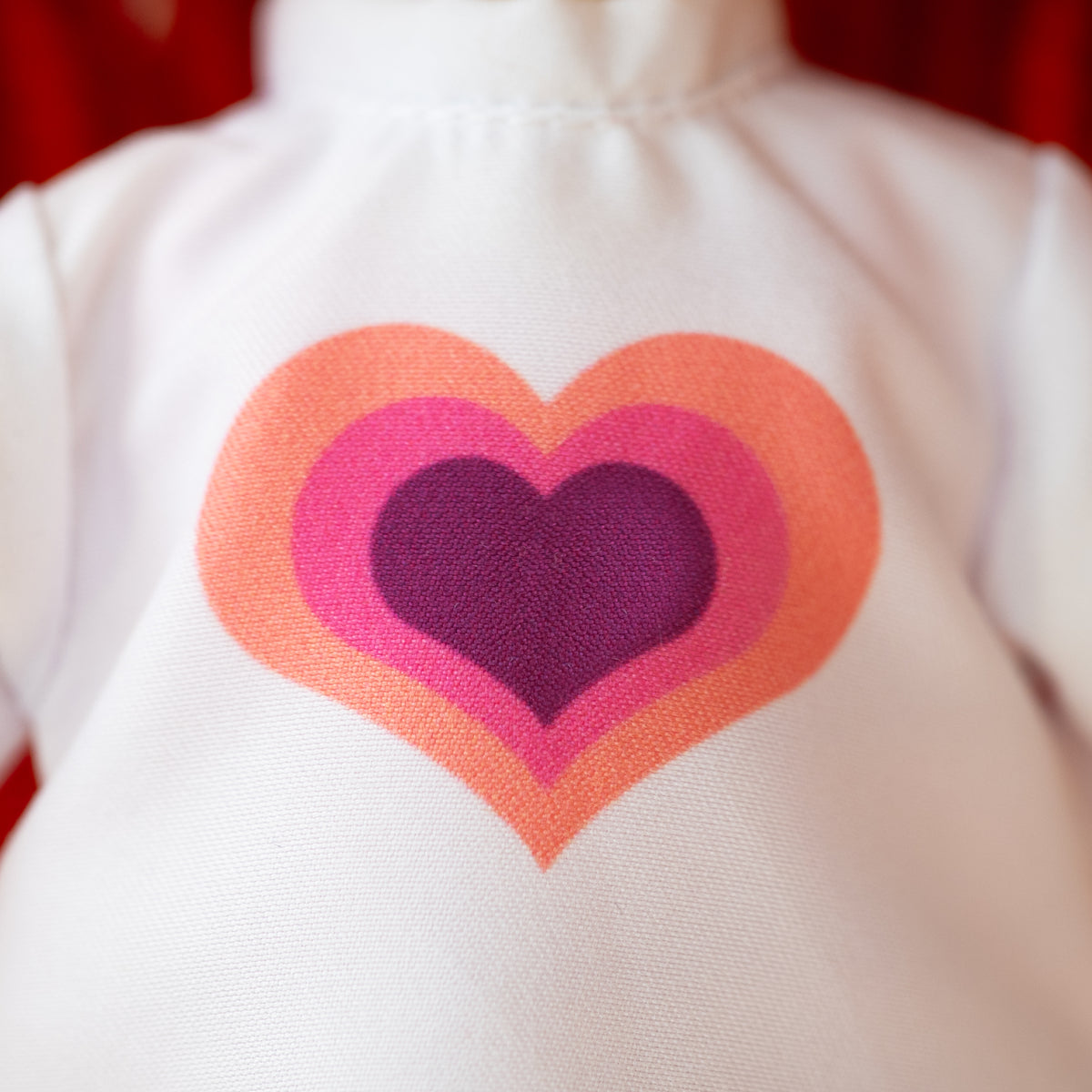 close up of a whilte doll t-shirt with a purple, pink, and orange heart.