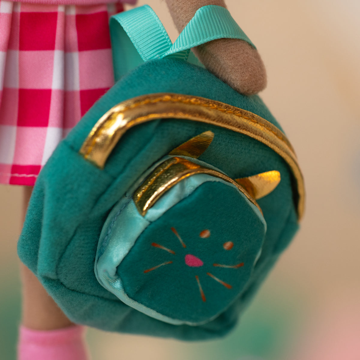close up of a soft doll holding a teal backpack with gold zippers and a kitty face and ears in the front