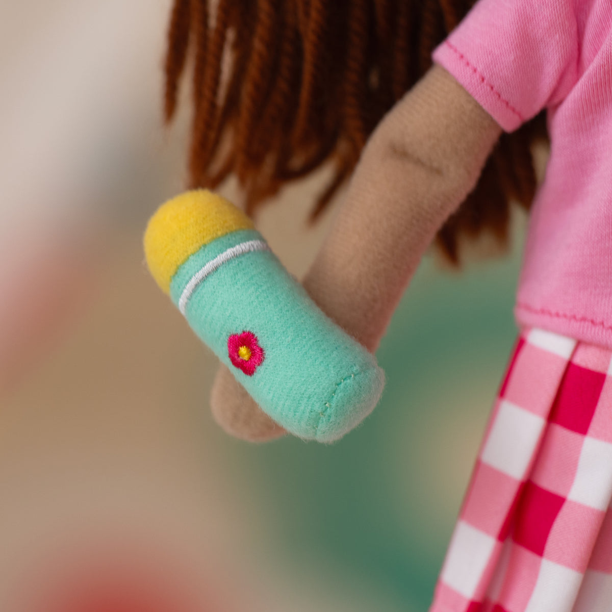 close up of soft doll holding a teal water bottle with a yellow lid and a pink embroidered flower