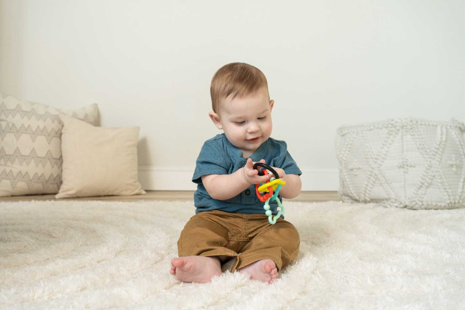 A baby sits on a rug holding multicolored bear-shaped rings in his hands.