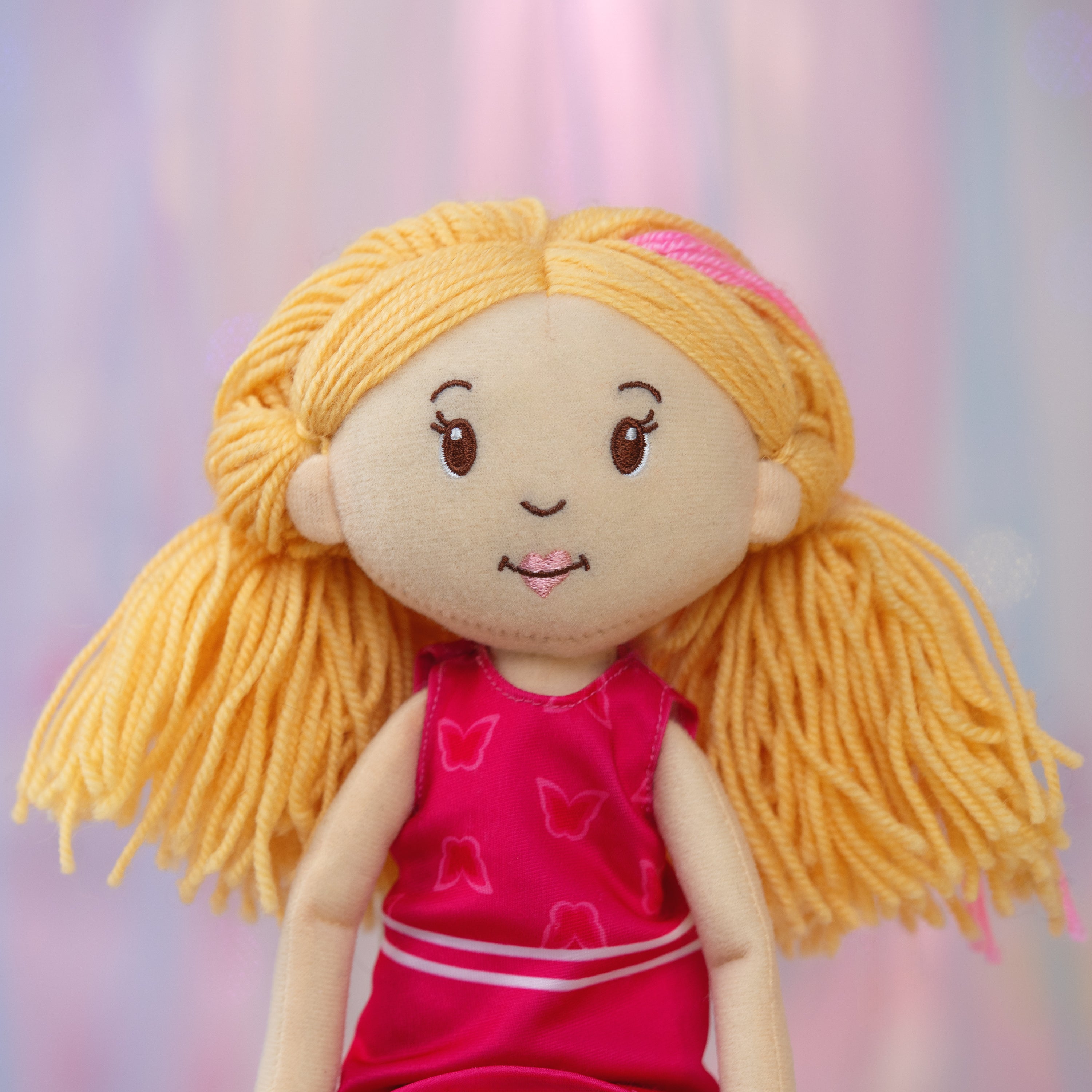Plush doll with blonde hair and a pink dress against a pink and purple background