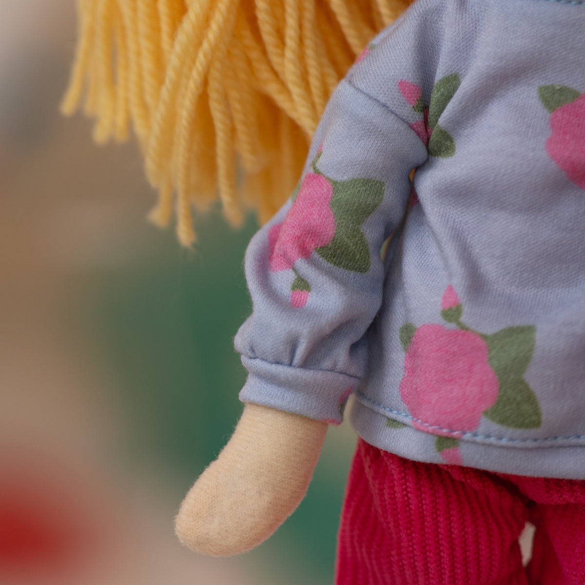 close up of soft doll wearing a floral patterned shirt with pink corduroy pants