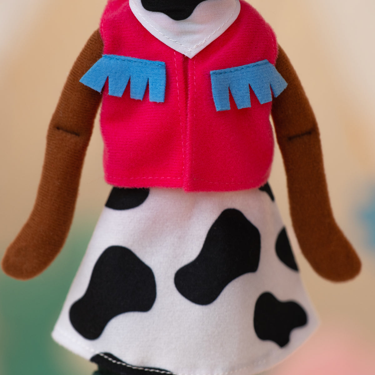 close up of soft doll wearing pink cowgirl vest with a cow print skirt and cow print bandana.