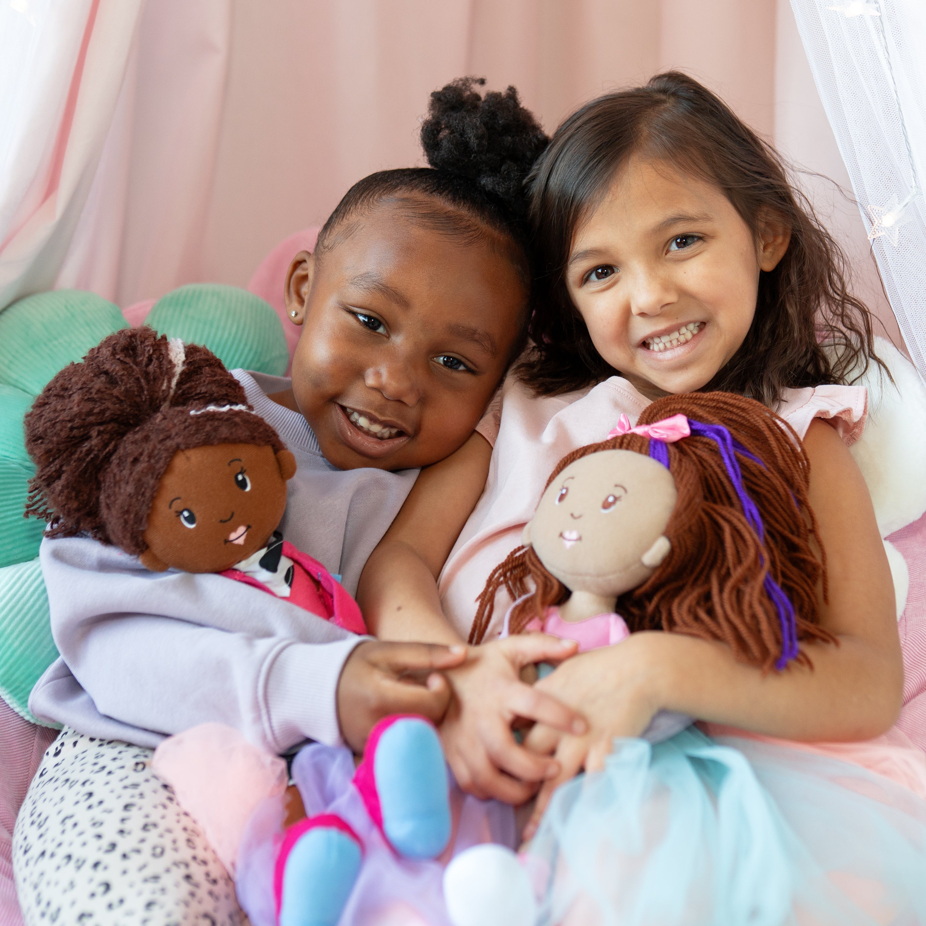 Two young girls holding dolls against a pink curtain background