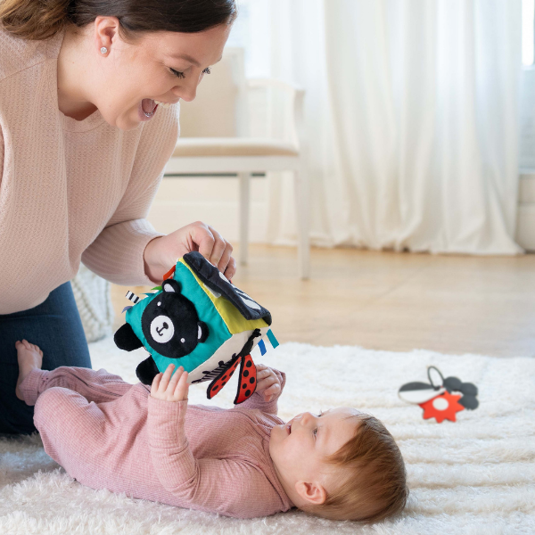 Woman playing with a baby on a rug, surrounded by toys.