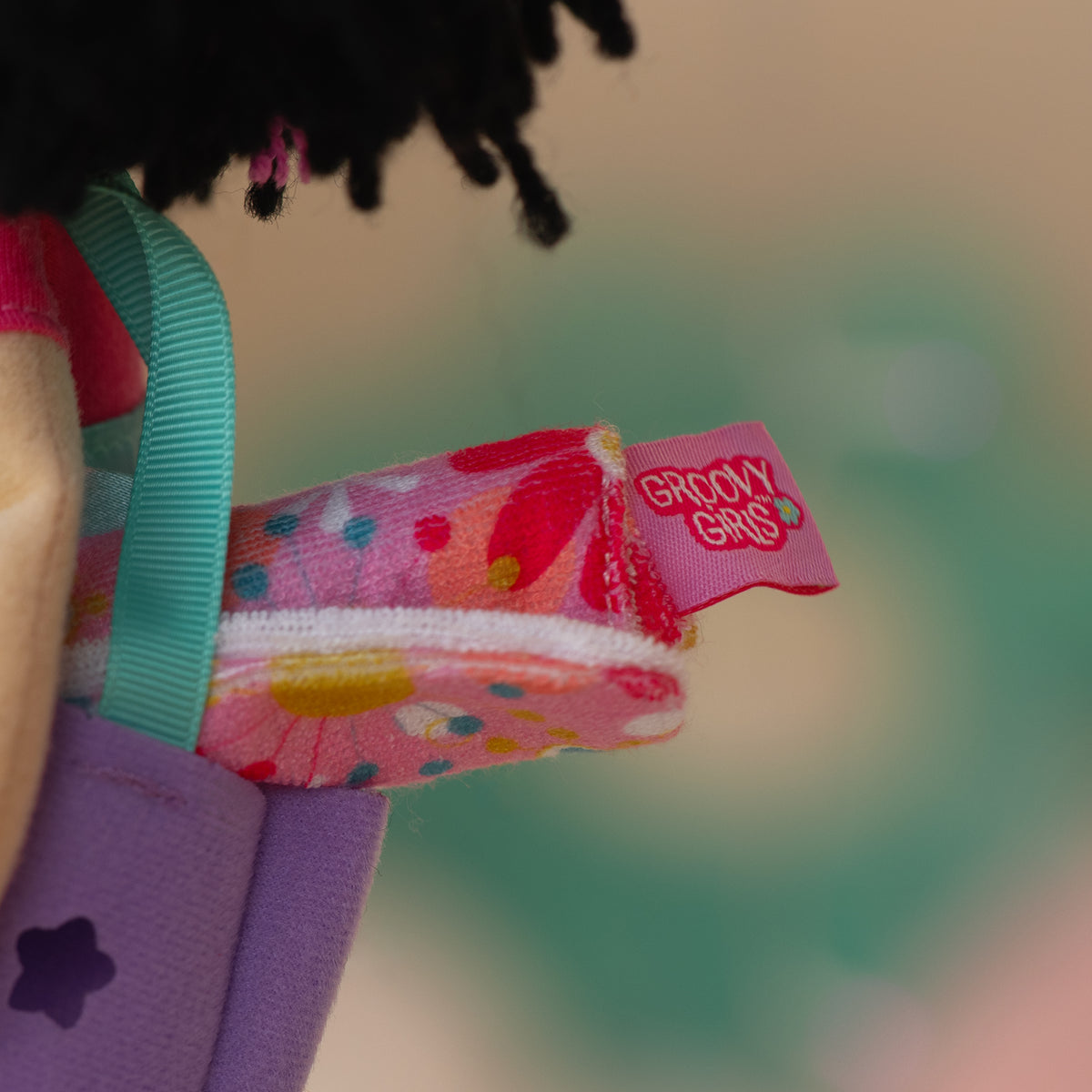 close up of a doll holding a purple bag with a pink floral towel inside it