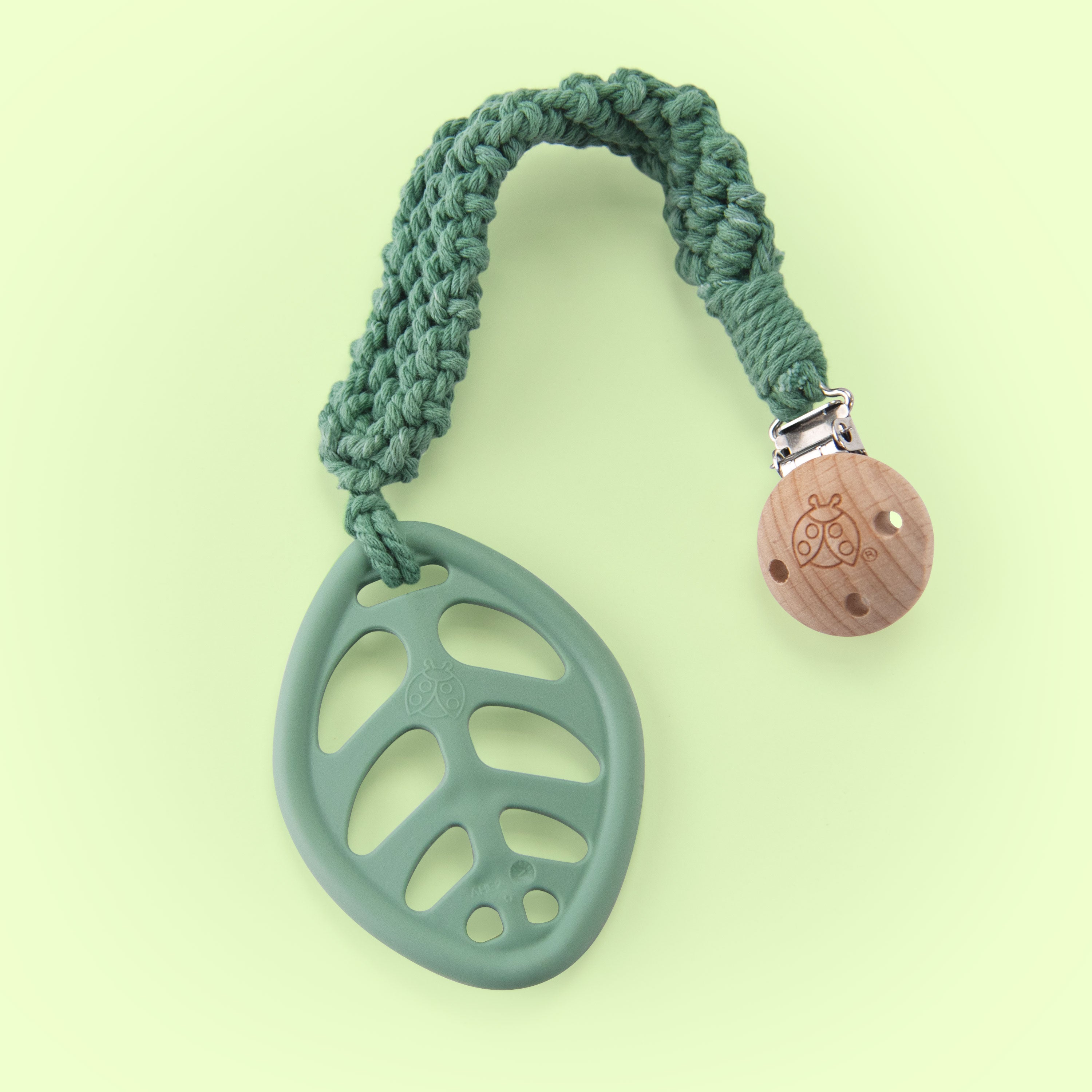 green leaf teether attached to a woven tether with a wooden clip all on a green background