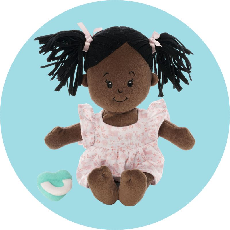 Seated brown skinned love, stella soft doll on a round blue background with a robins-egg-blue colored doll pacifier nearby.