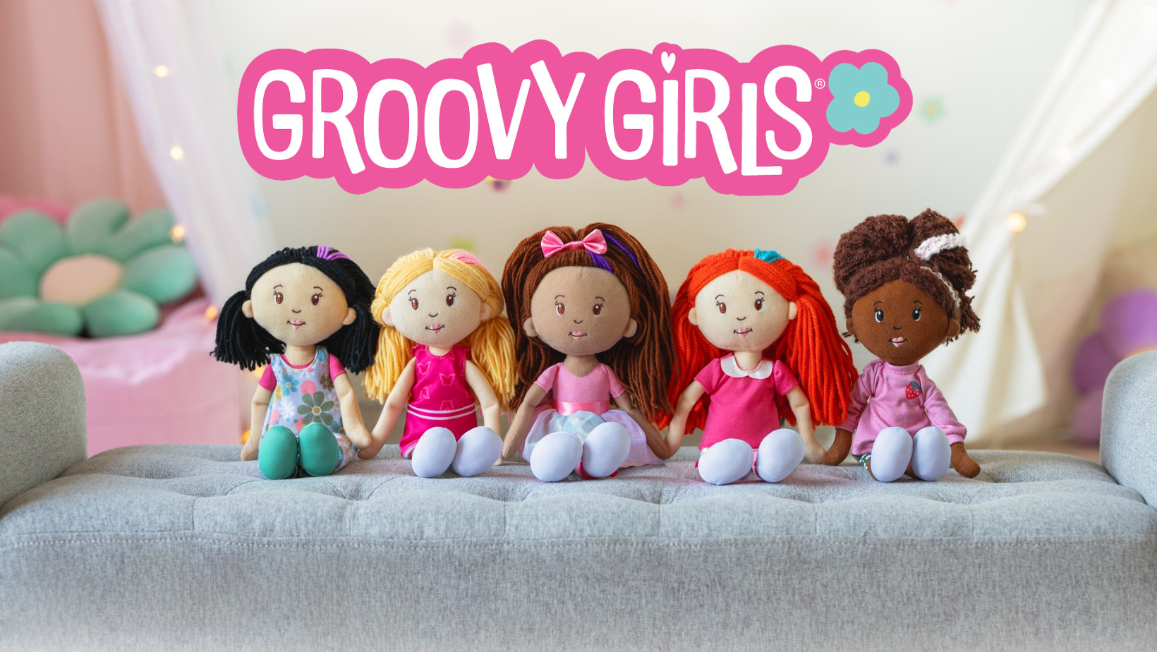Five soft dolls seated on a bench in a room scene with Groovy Girls logo positioned above. 
