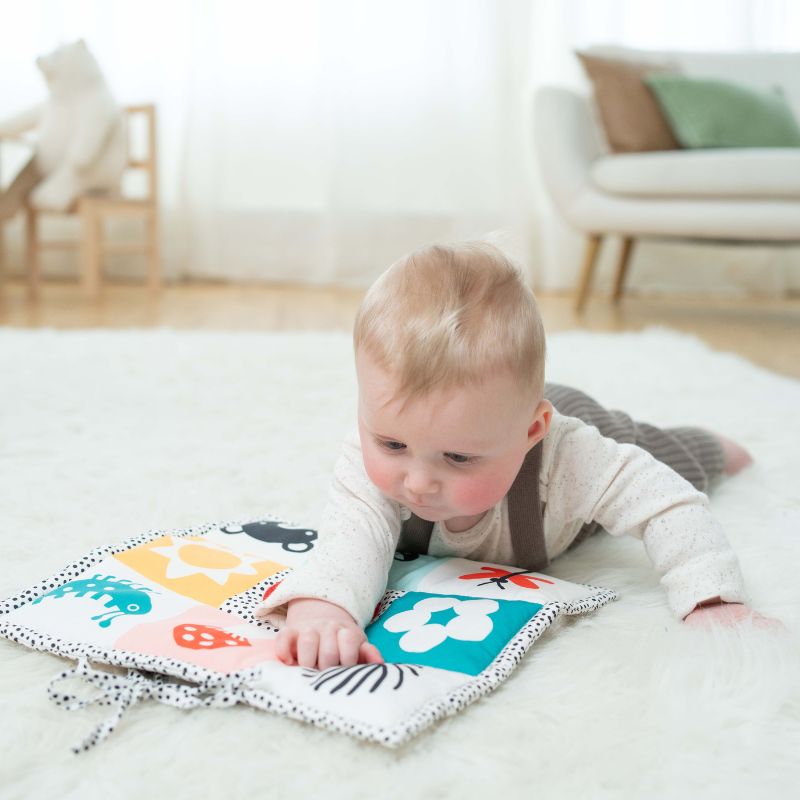 Baby boy lying on his tummy on a colorful tummy time mat laid on a plush white rug in a living room scene. Baby's arm is outstretched on the mat as he gazes at the graphics. 