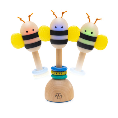 Three Brilliant Bee baby rattles showing glowing color modes with yellow wings and a wooden base with colorful rings.