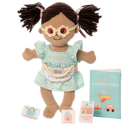 Wee Baby Stella doll wearing glasses and a dress, with a toy adventure book and location cards.