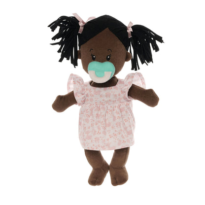 brown skinned soft baby doll with black pigtails in a pink dress with a blue magnetic pacifier attached to the doll's face