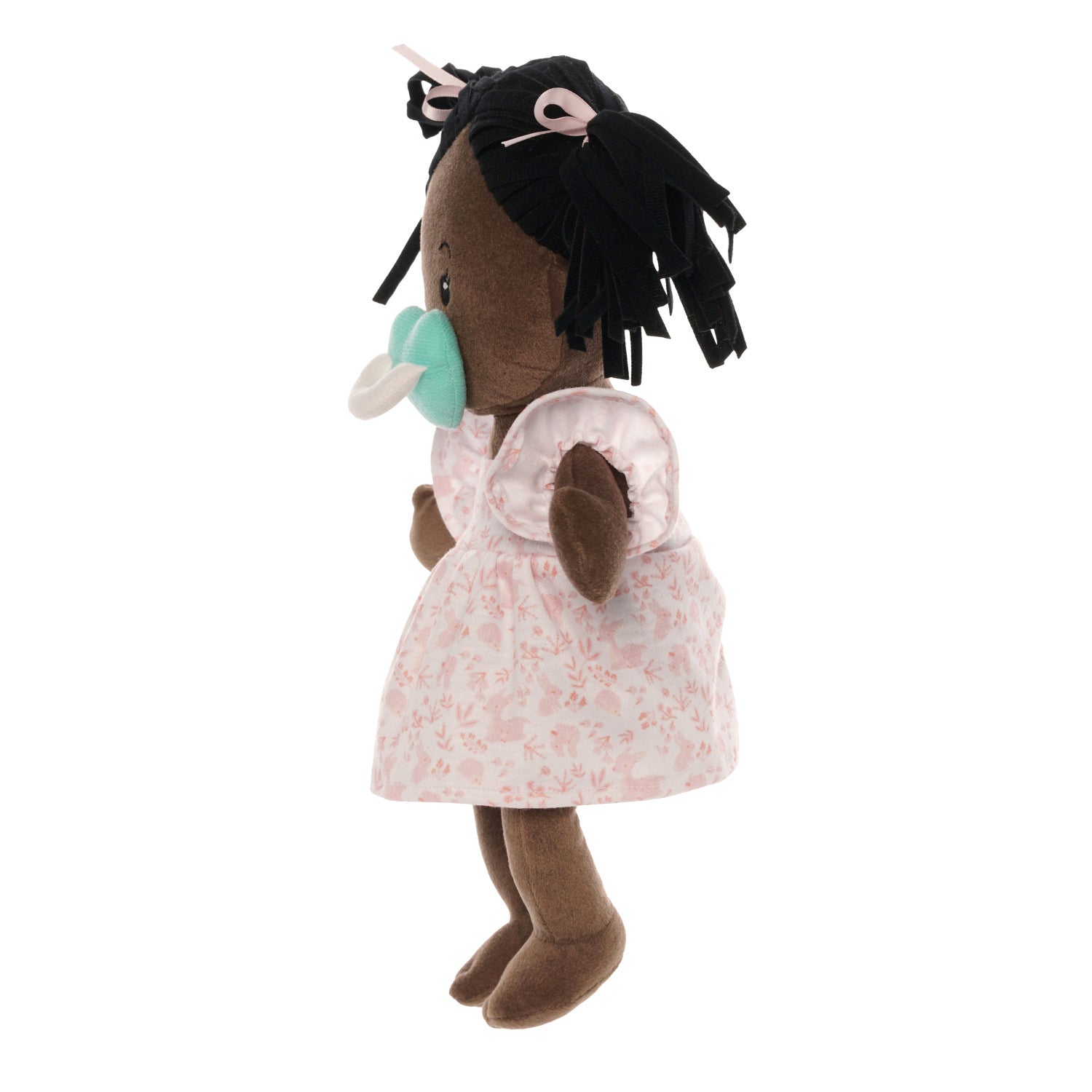 brown skinned soft baby doll with black pigtails in a pink dress with a blue magnetic pacifier attached to the doll's face