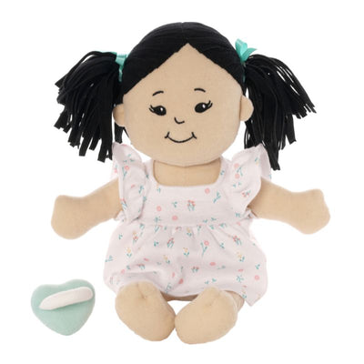 Soft doll in a seated position with black hair and light beige skin wearing a dress with a light green magnetic pacifier seated next to the doll.