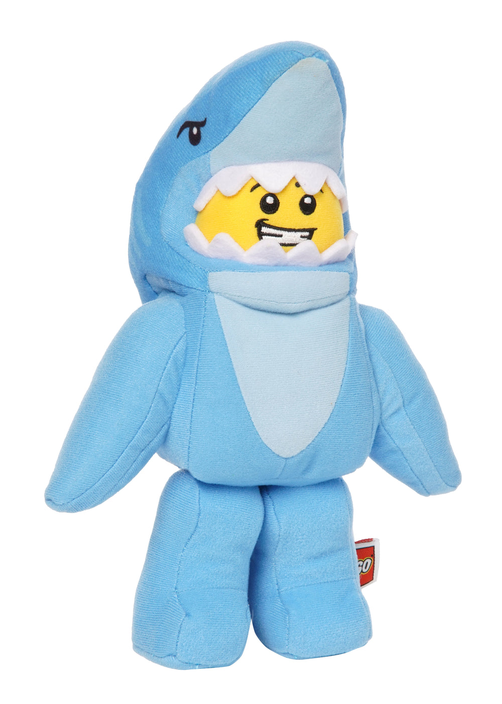 Light blue shark costume plush inspired by LEGO shown in front view with a grinning yellow face framed by soft white teeth.