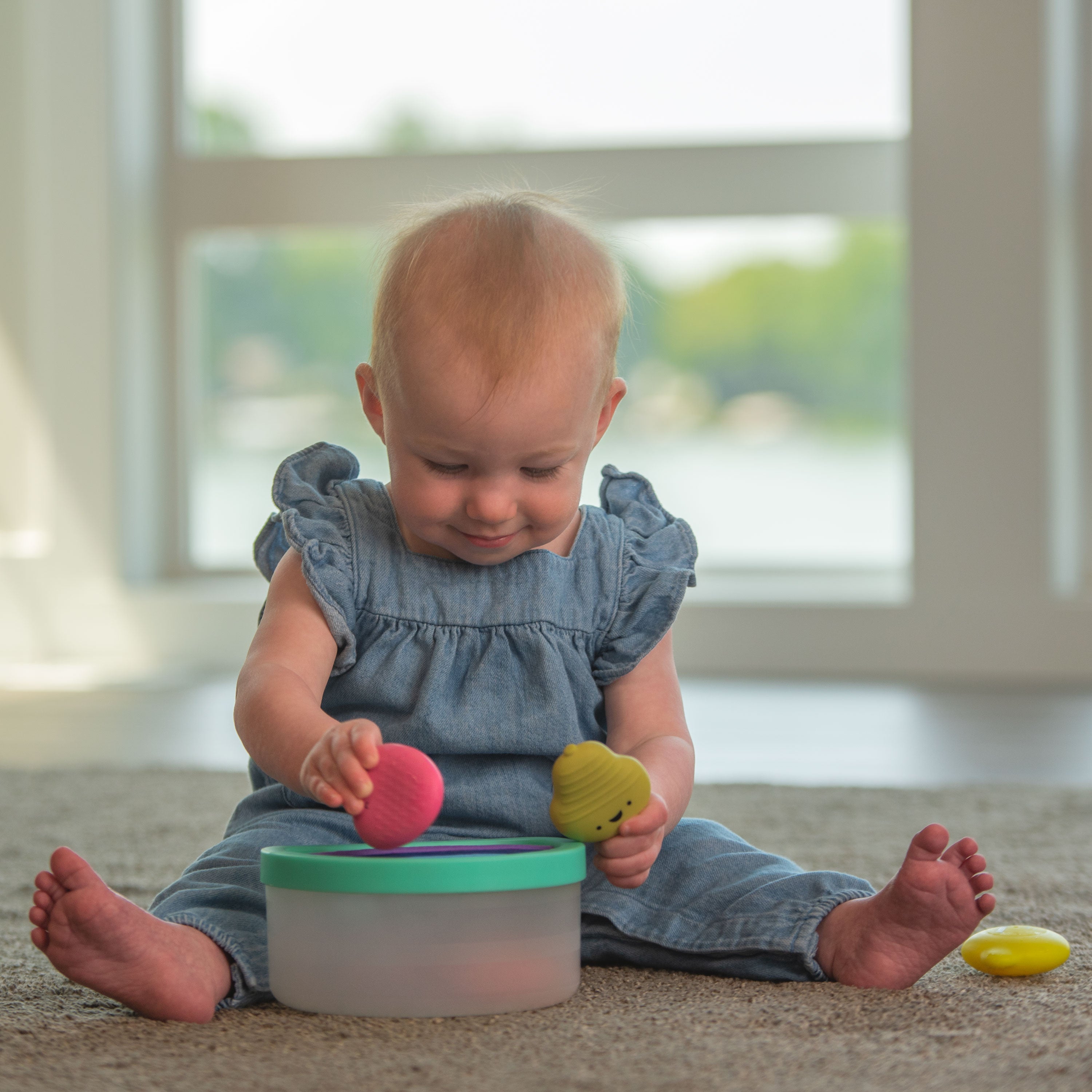 Baby playing with a container and toys on a carpeted floor.