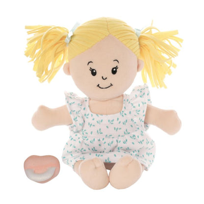 Peach skinned soft doll in a seated position with blonde hair pigtails wearing a dress with a pink pacifier seated next to the doll. 