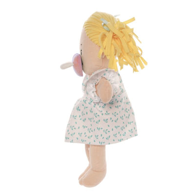 Peach skinned soft doll in a standing 
 side profile position with blonde hair pigtails wearing a dress with a pink pacifier on the face of the doll. 