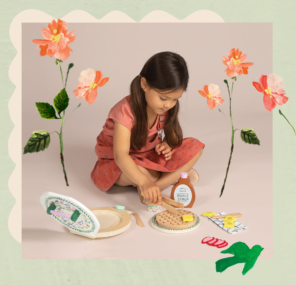Little girl sitting on ground, playing with waffle and butter toys