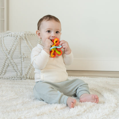 Baby sitting on a soft rug while playing with a colorful textured teether toy.