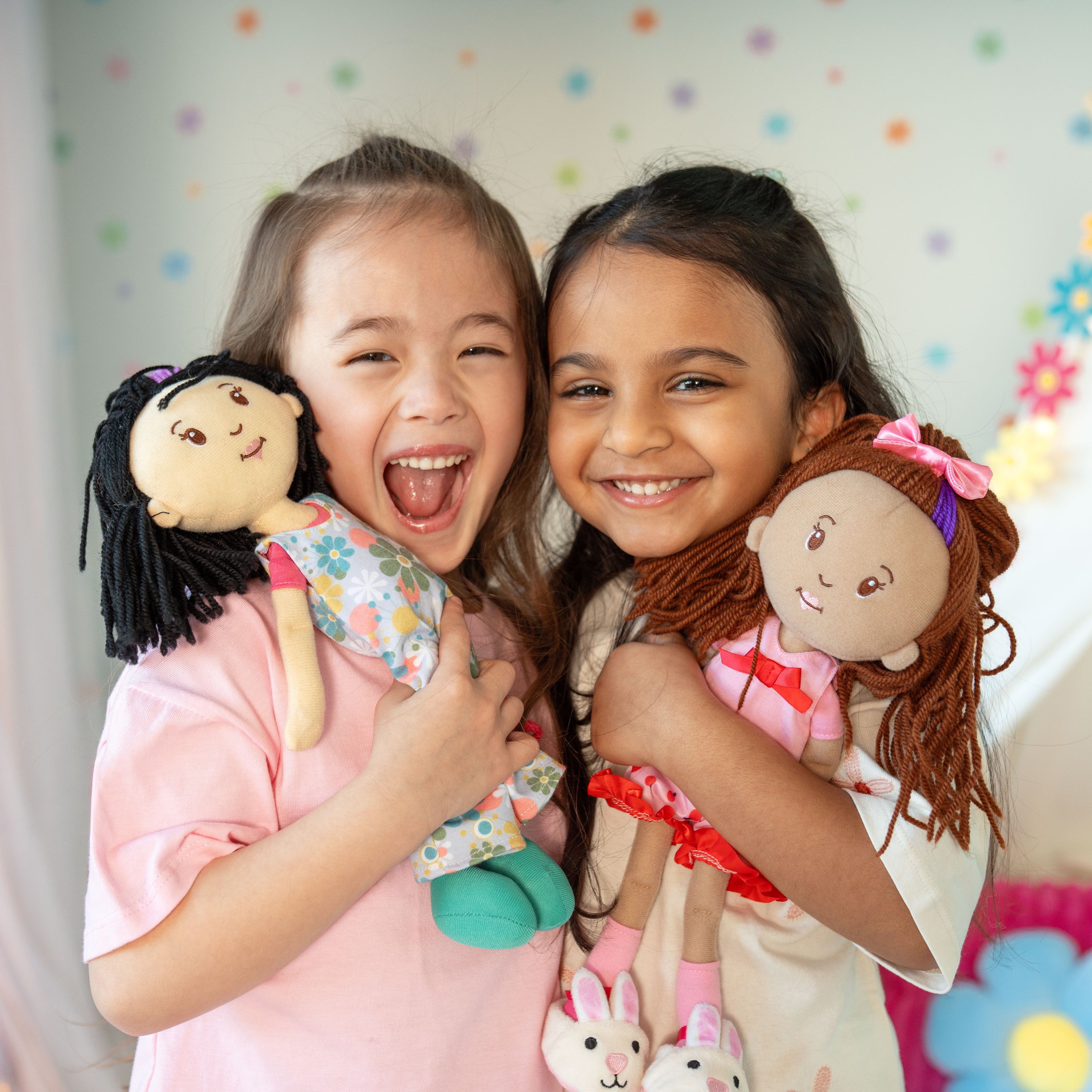 Two children holding dolls against a colorful polka dot background