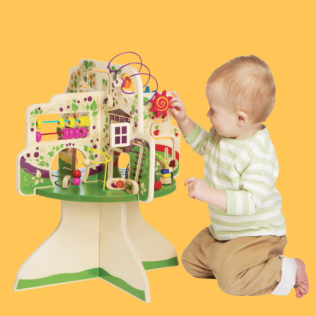 Toddler playing with a colorful activity table featuring beads and tracks, on a yellow background.