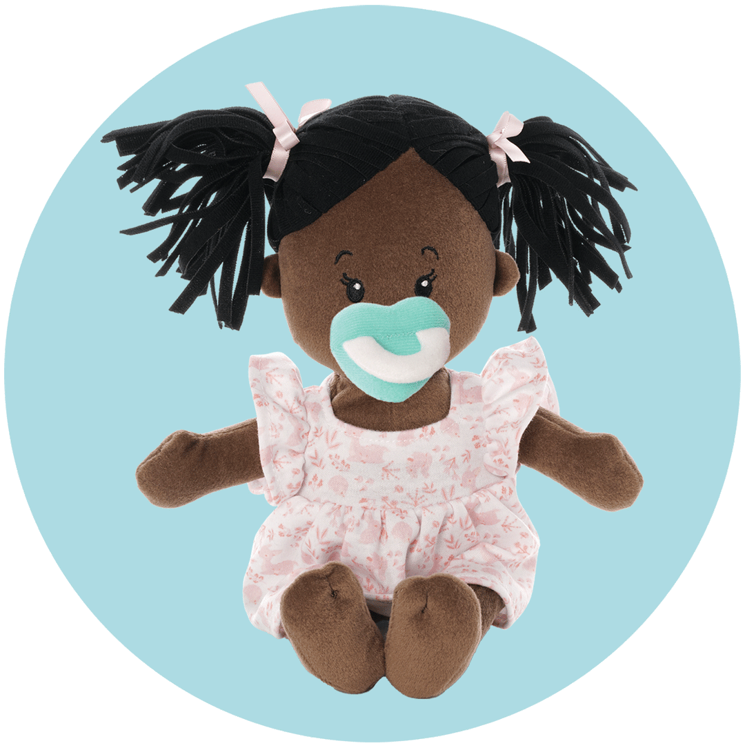 Plush baby doll with dark hair in pigtails, wearing a pink floral dress and holding a teal pacifier, set against a light blue background.
