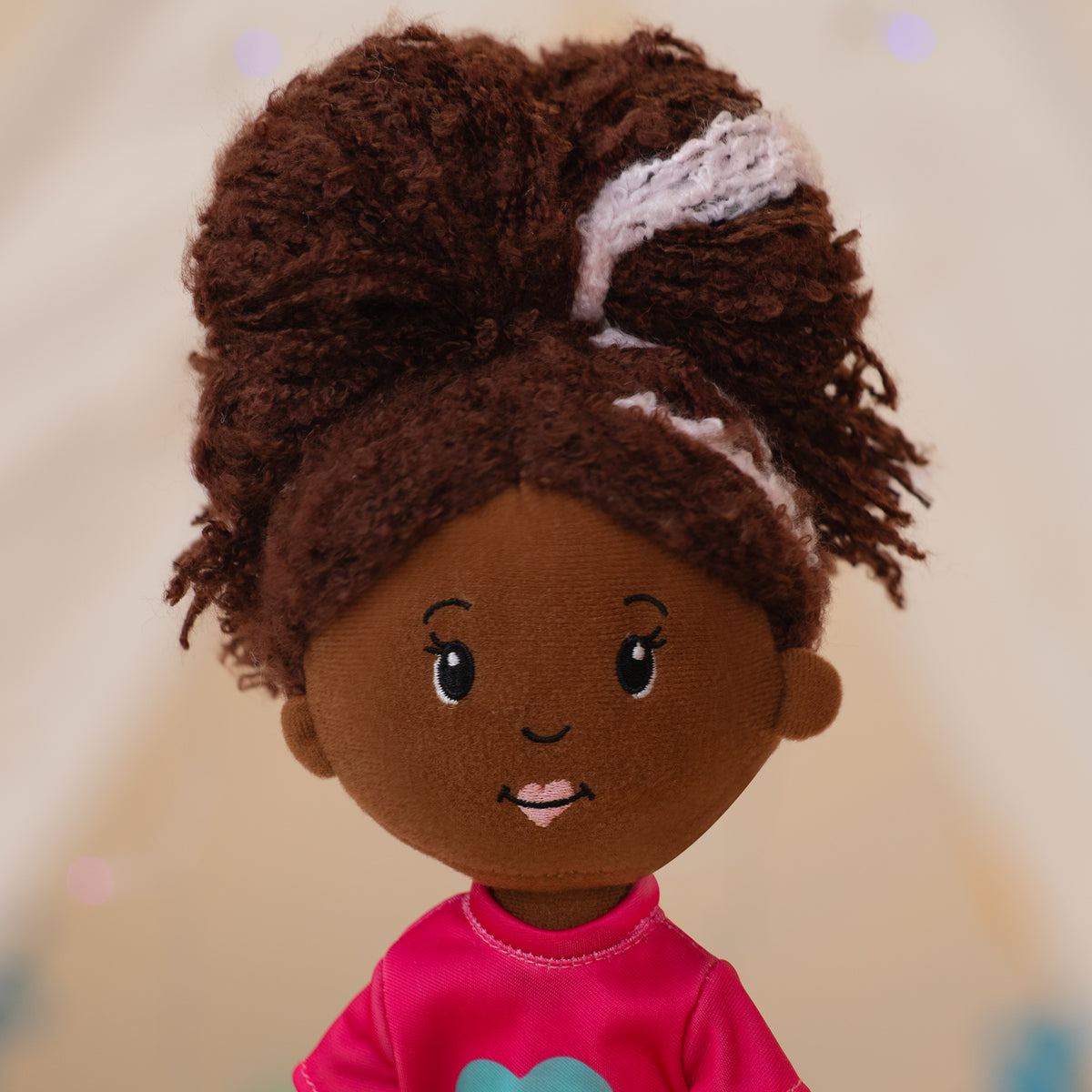 close up of soft doll wearing a pink shirt with a blue flower