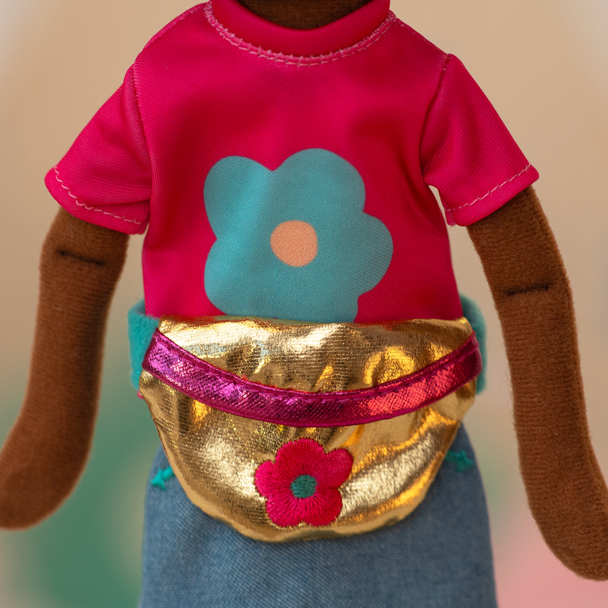 close up of a soft doll wearing a pink shirt with a blue flower, jean skirt, and a golden waist bag with a pink flower