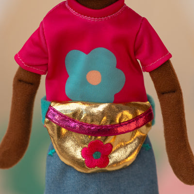 close up of a soft doll wearing a pink shirt with a blue flower, jean skirt, and a golden waist bag with a pink flower