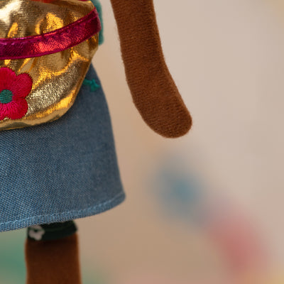 close up of a soft doll wearing a jean skirt and golden waist bag with a pink flower
