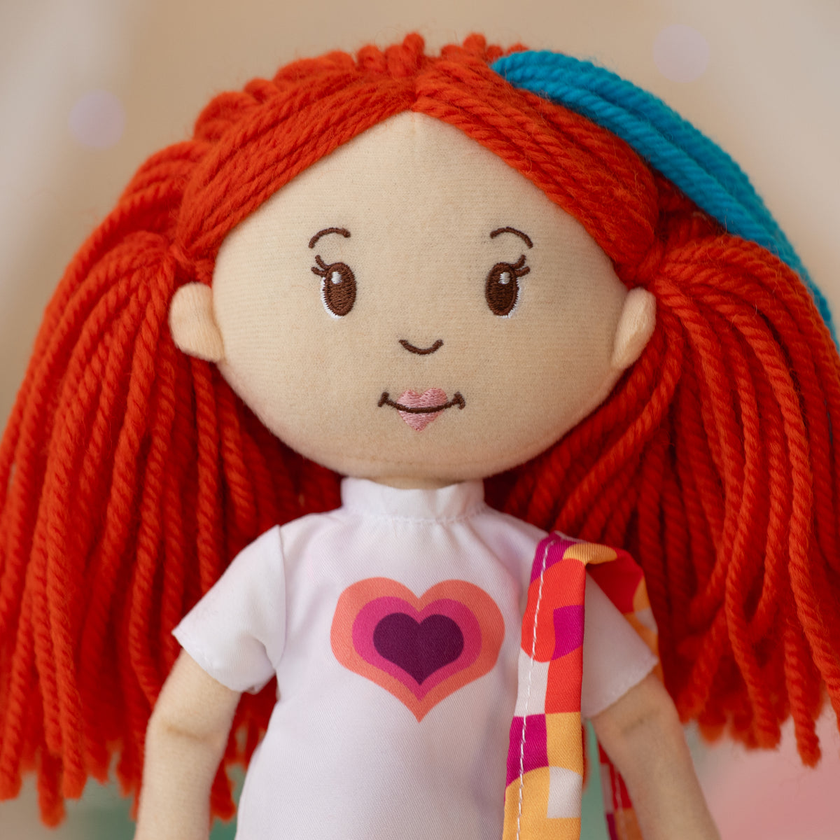 close up of soft doll wearing a white t-shirt with a colorful heart, holding a colorful purse on one shoulder