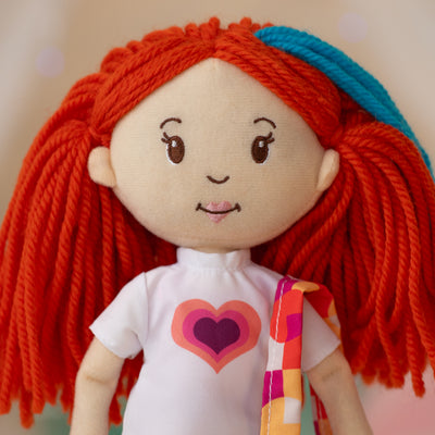 close up of soft doll wearing a white t-shirt with a colorful heart, holding a colorful purse on one shoulder