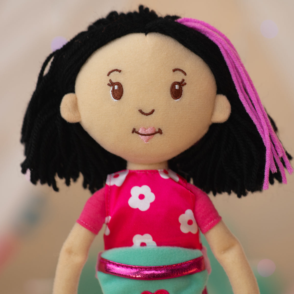 close up of a soft doll wearing a pink and white floral shirt with a teal waist bag