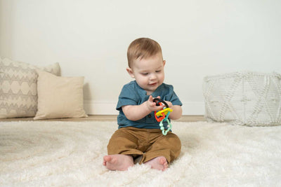 A baby sits on a rug holding multicolored bear-shaped rings in his hands.
