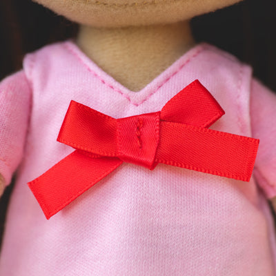 close up of soft doll wearing pink pajama shirt with a red bow