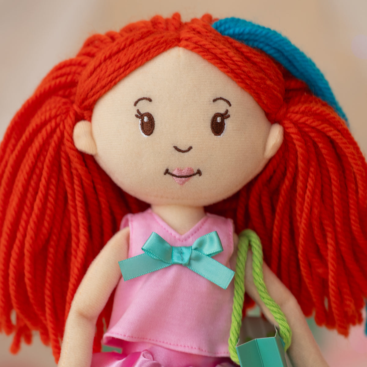 close up of soft doll wearing a pink shirt with blue bow, holding a gift bag
