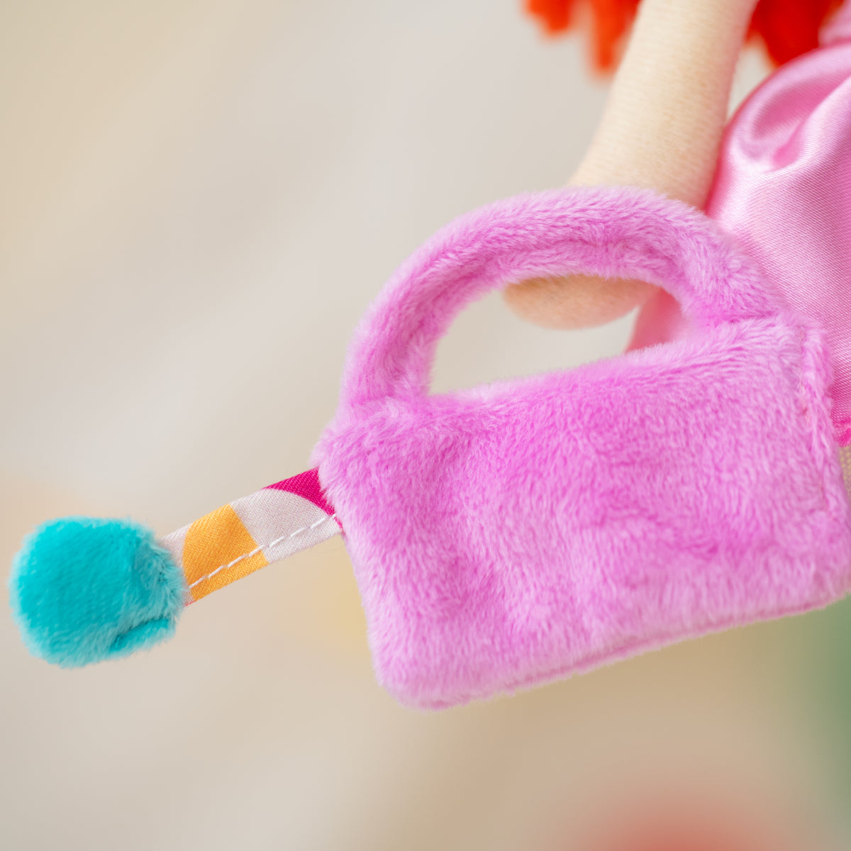 A close-up of a small plush pink purse held by a doll. 
