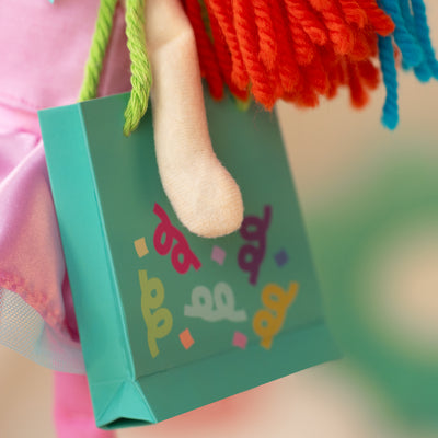Close up of a teal gift bag with colorful confetti design, held by a soft doll