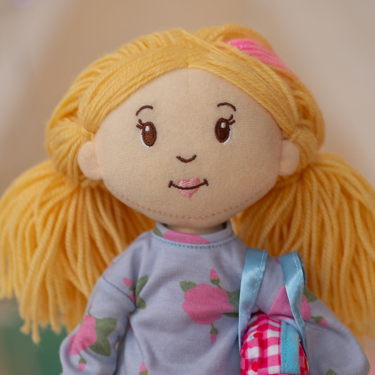 close up of soft doll wearing floral patterned shirt holding a pink duffel bag