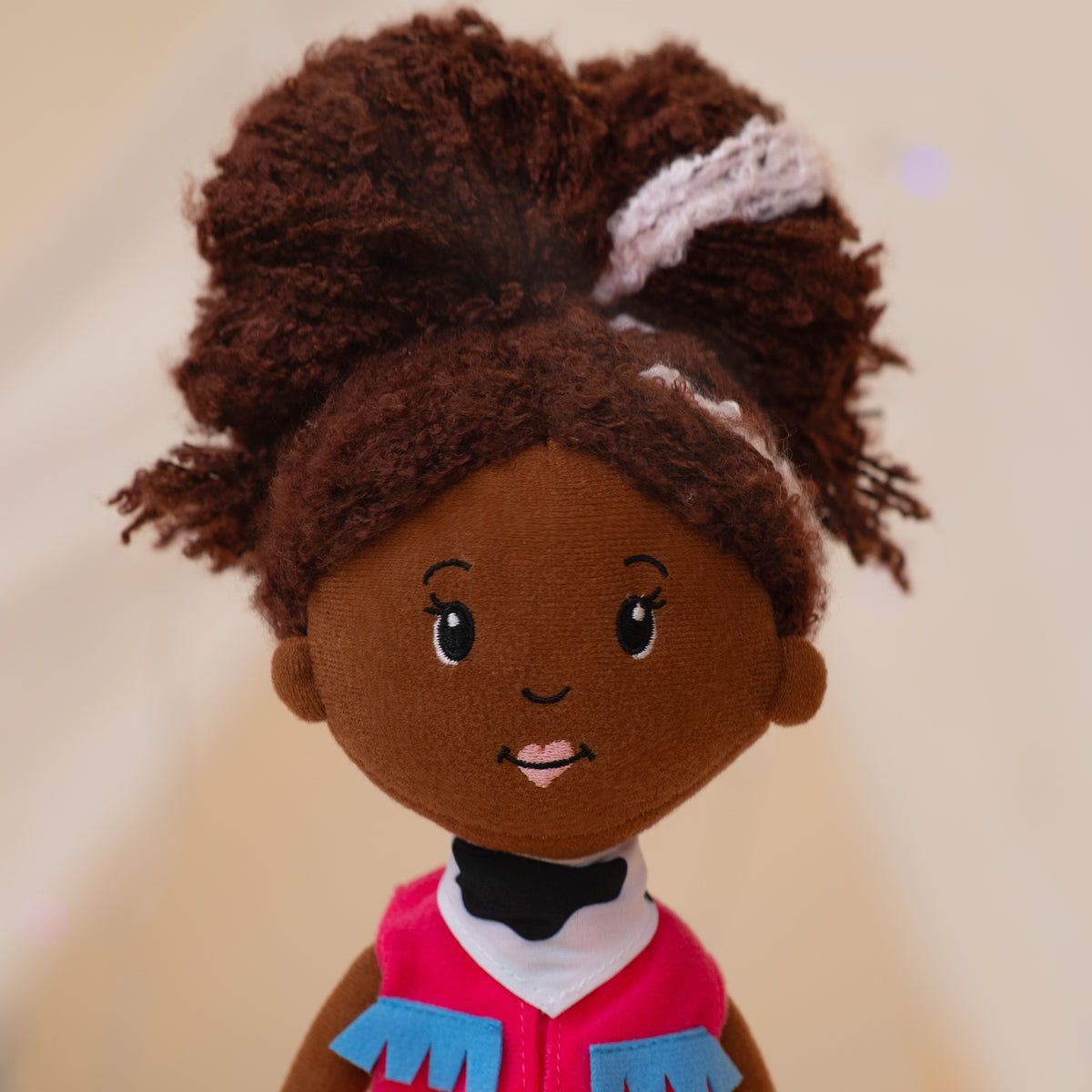 close up of soft doll wearing pink cowgirl vest and cow print bandana