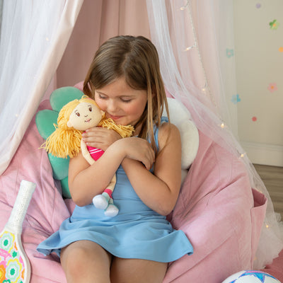 Young girl holding a plush toy in a cozy room with pink bean bag and decorative lights.
