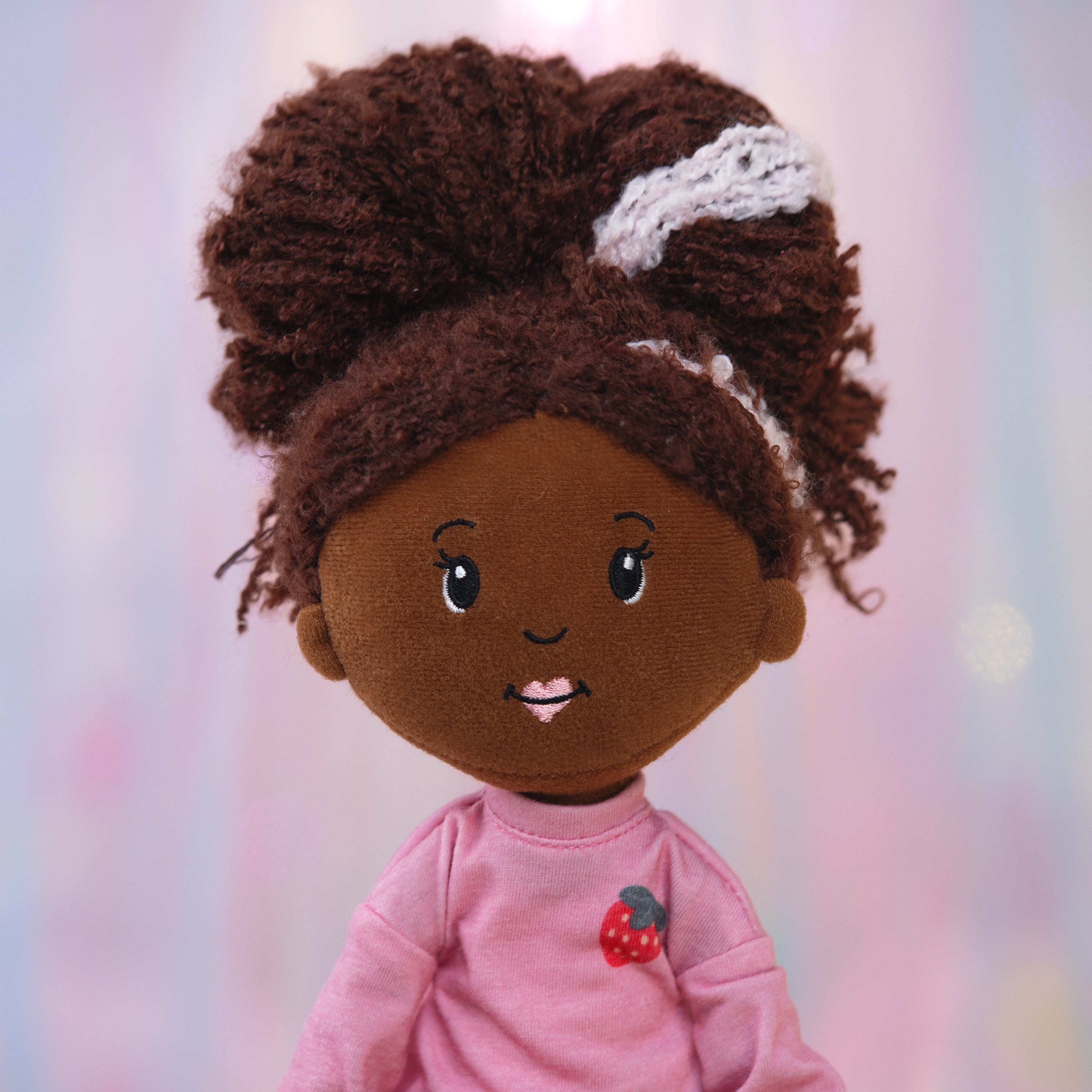 Plush toy of a girl with brown hair and pink shirt on a light pink and purple background